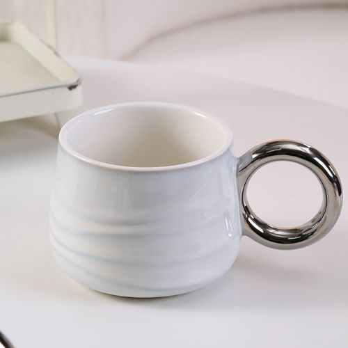 Bijela Keramička Šalica Urban Ripple s keramičkom ručkom srebrne boje, prikazuje valoviti uzorak i sjaj u detaljnom prikazu.