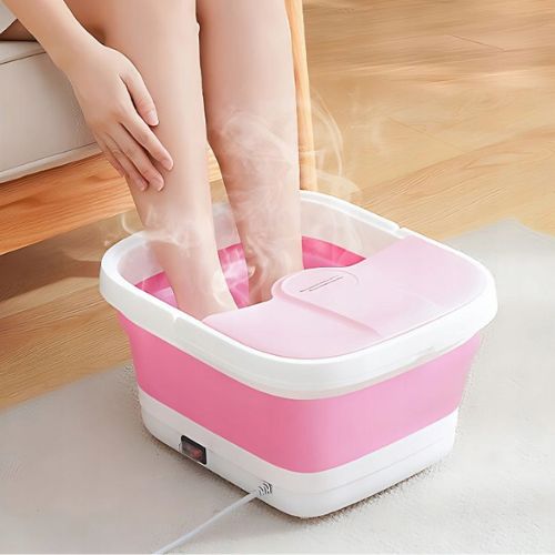 Žena koristi ružičasti sklopivi masažer za stopala u dnevnom boravku; iz masažera izlazi para koja prikazuje funkciju grijanja vode